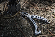 Leatherman Skeletool multi-tool on gravel with blades extended near camping gear