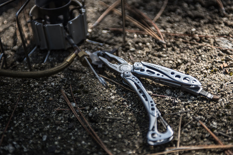 Leatherman Skeletool multi-tool on gravel with blades extended near camping gear