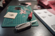 Stainless steel multi-tool with blades and handles, closed on work surface