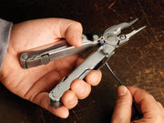 Stainless steel multi-tool held in hand, plier jaws and tools visible
