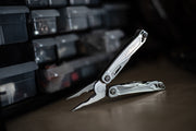 Stainless steel multi-tool, open with pliers and blade on dark workshop floor