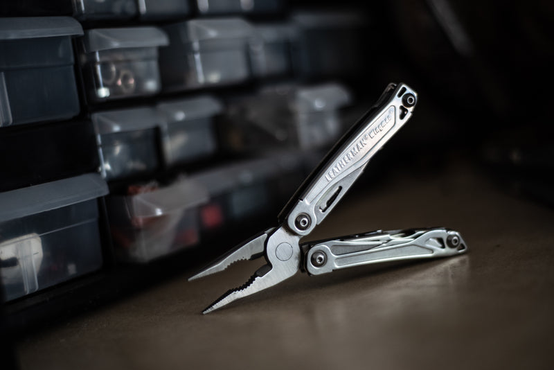 Stainless steel multi-tool, open with pliers and blade on dark workshop floor